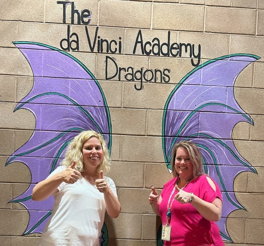 Principal Freeman-Todd and Assistant Principal Landon pose in front a wall painted with dragon wings.